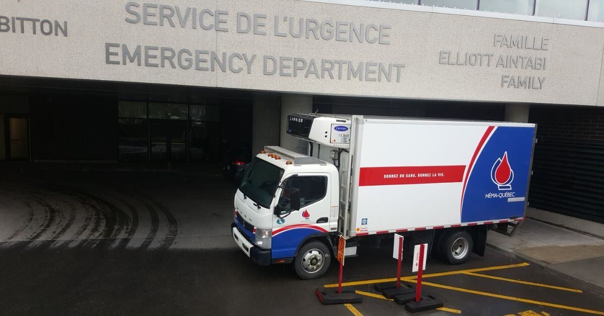 Héma-Québec refrigerated transport truck parked in front of an emergency department, showcasing cold chain logistics.