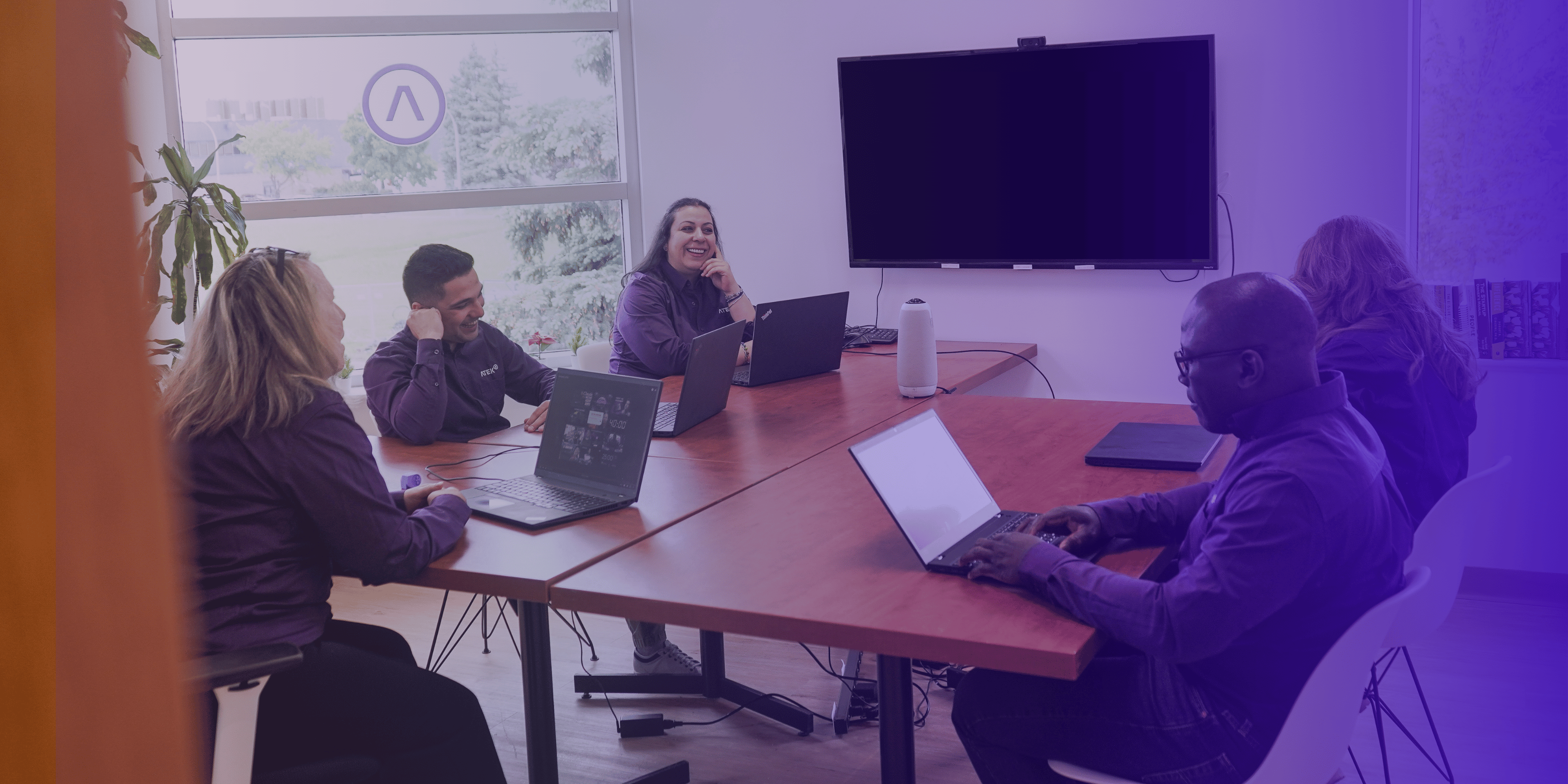 ATEK team in a collaborative meeting around a table, working on laptops.